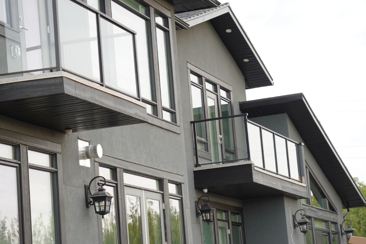 Modern gray house with large windows and glass balcony.
